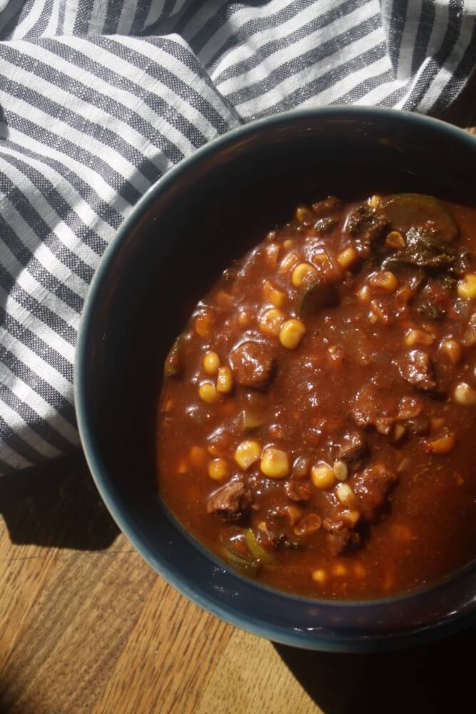 overhead view of beef vegetable stew in blue bowl with striped towel