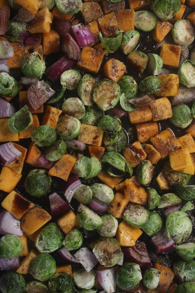 aerial view of butternut squash, brussels sprouts, and red onion chopped and mixed on sheet pan