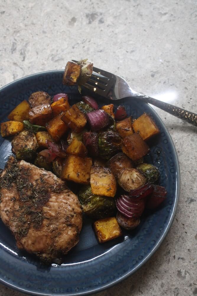 baked chicken, brussels sprouts, butternut squash, and red onion on blue plate with fork